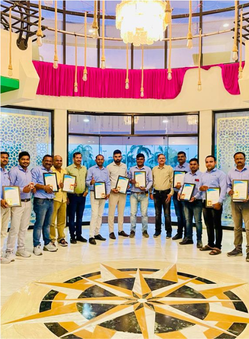 Global agro team posing in a yellow lit hotel lobby with certificates.