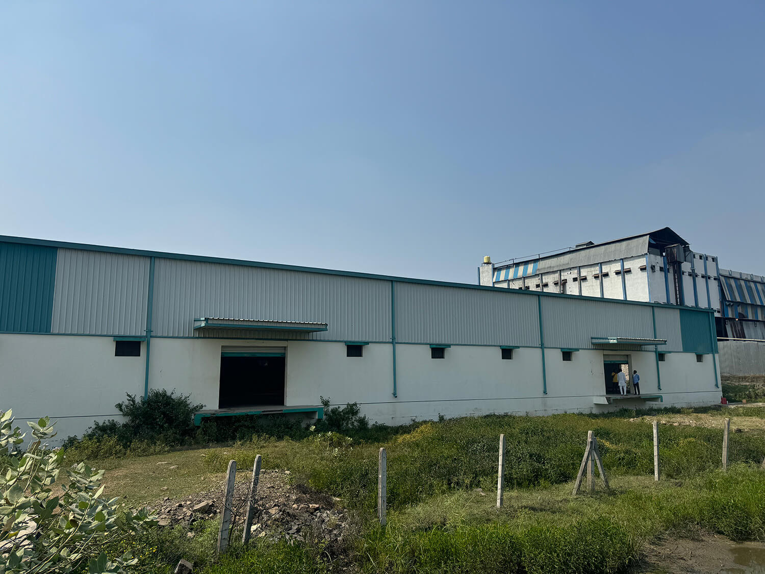 Large metal warehouse building with a chain-link fence in front. Clear blue sky in the background.