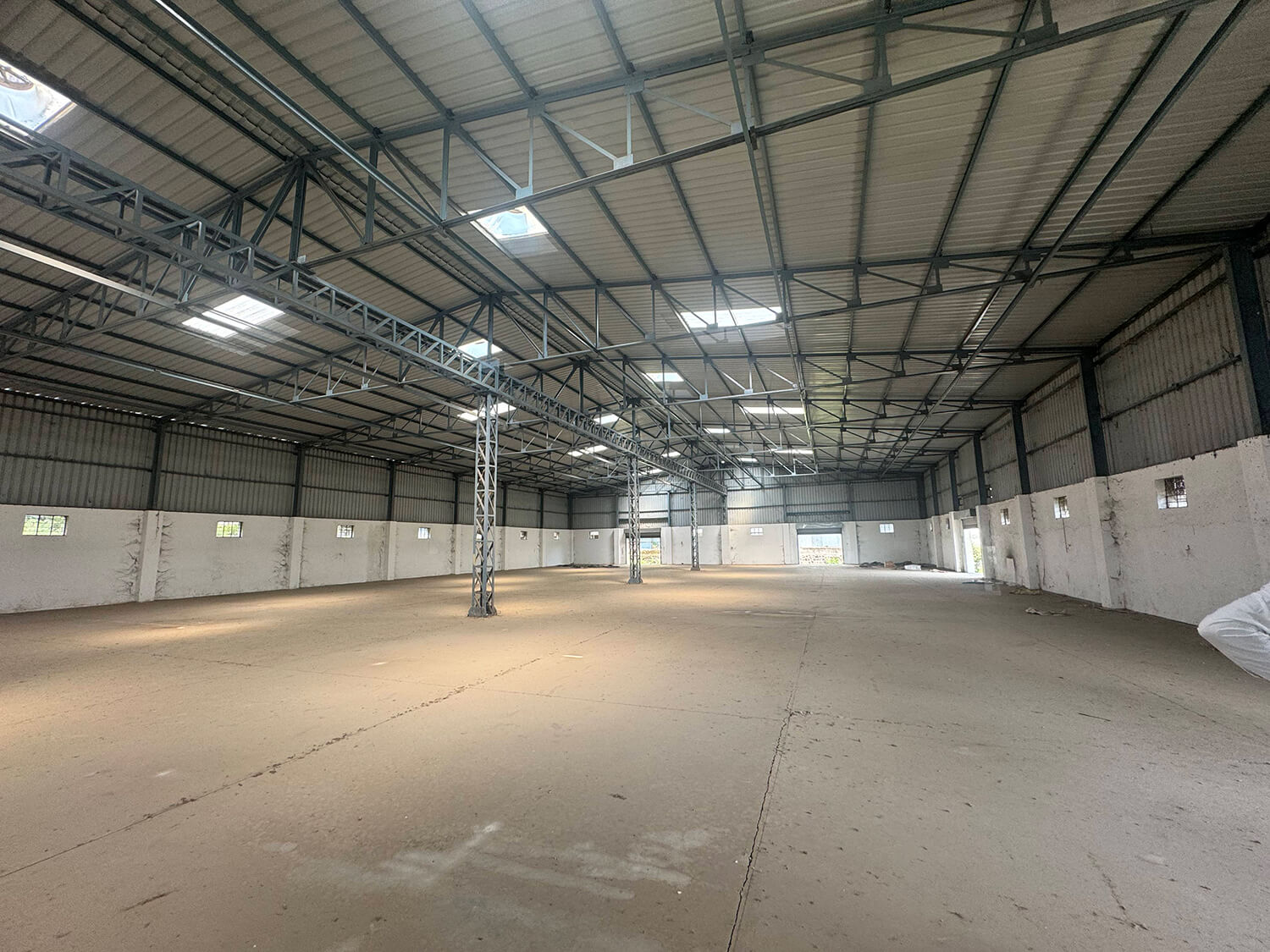 Empty industrial warehouse interior with large metal ceiling fan. Sunlight streams through high windows.